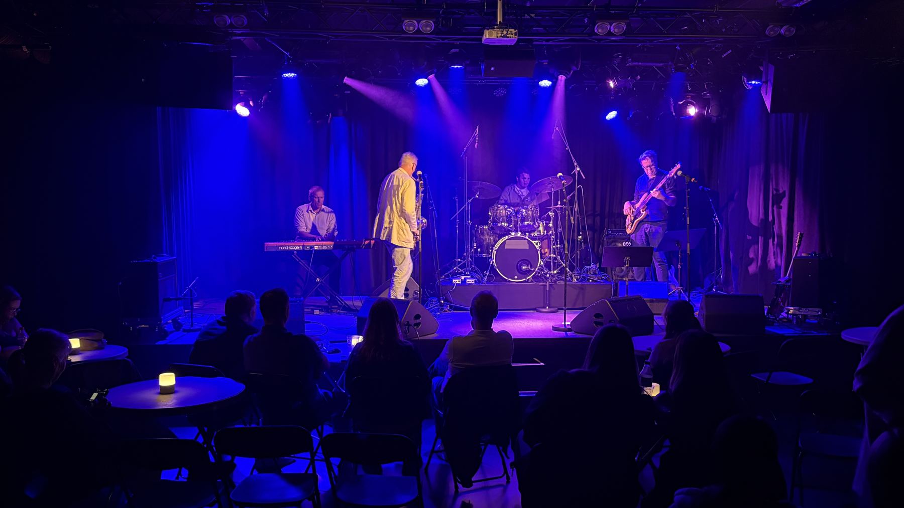 Jam-bandet på scenen på Kulturhuset i Hamar, med publikum ved bordene foran scenen